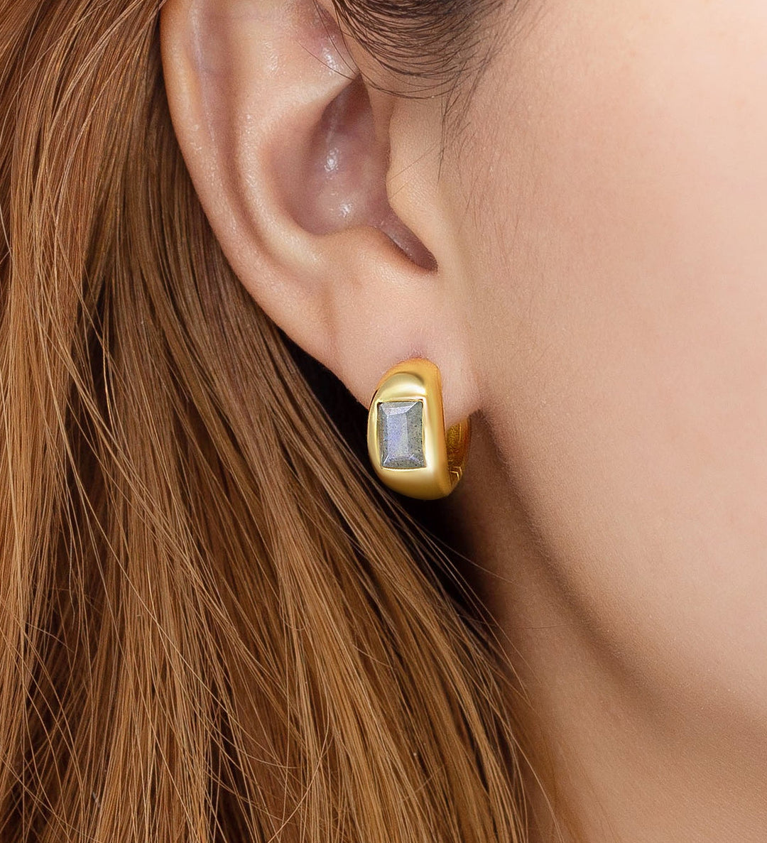 Gold earring with a gemstone worn by a person with brown hair.