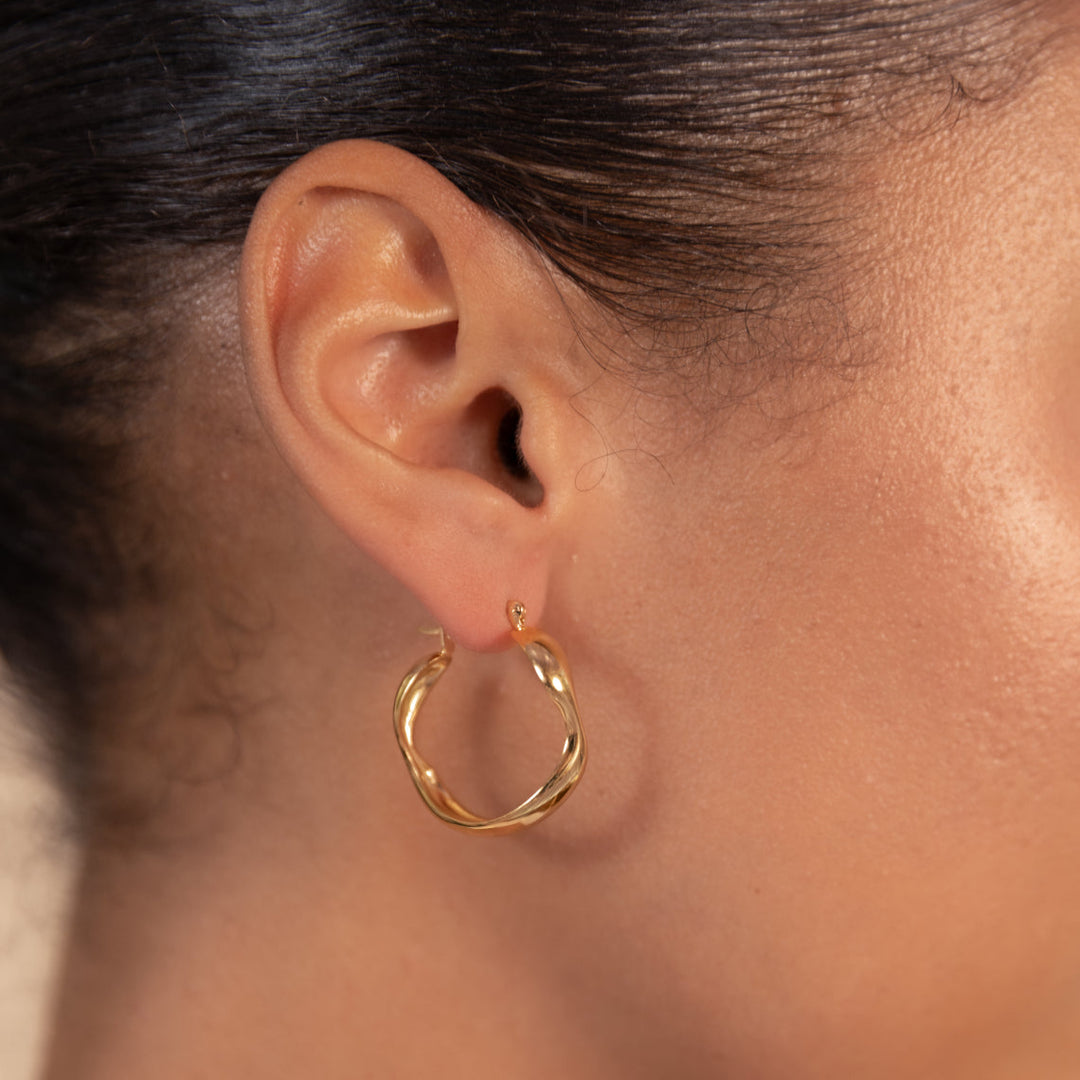 Close-up of a person wearing gold hoop earrings with a neutral background