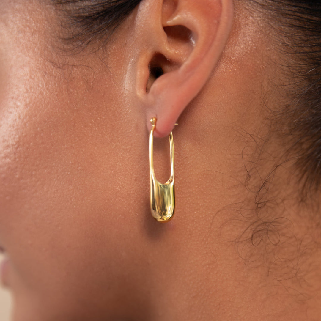 Gold hoop earring worn by a person with a neutral background